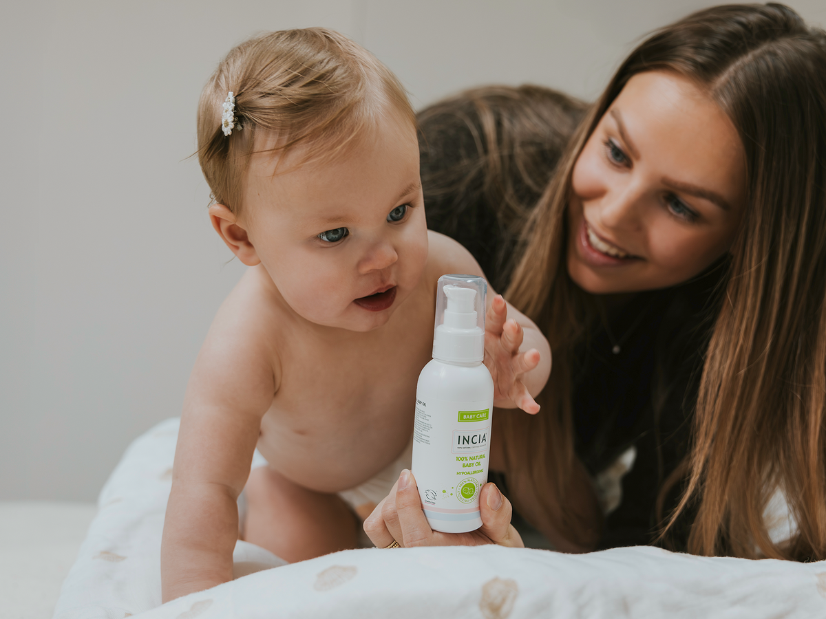 Lachende ouder met baby die reikt naar een fles INCIA Natuurlijke Baby Olie